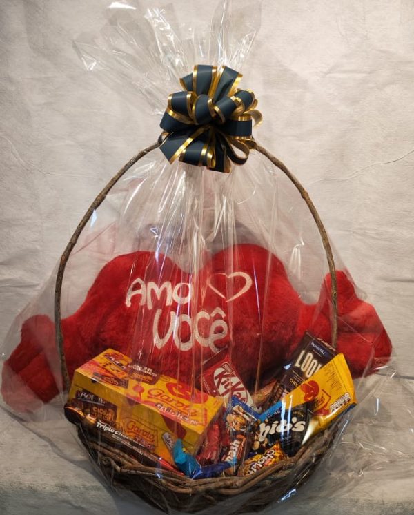 Imagem de uma cesta generosa de chocolates variados, decorada com um coração de pelúcia. A cesta transmite uma sensação de carinho e doçura, representando um presente especial para momentos afetuosos.